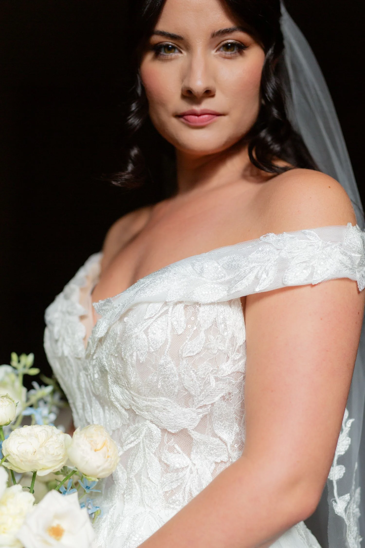 Bride in an off-shoulder lace gown beside white ranunculus