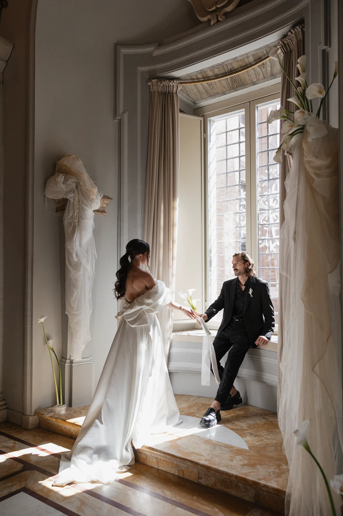 Couple by a tall window with white drapery and a sculptural floral column