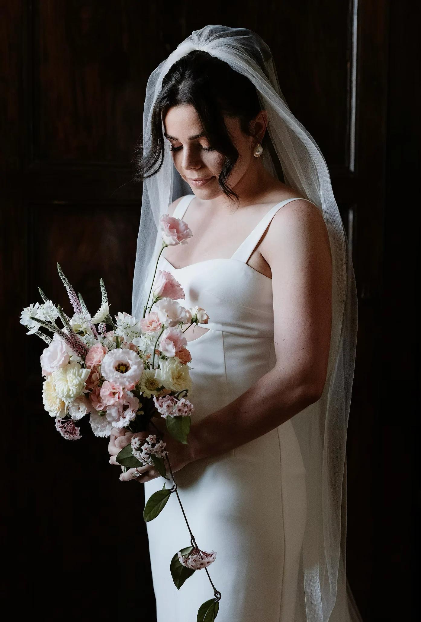 Bride in a veil holding a blush and cream bouquet in low light