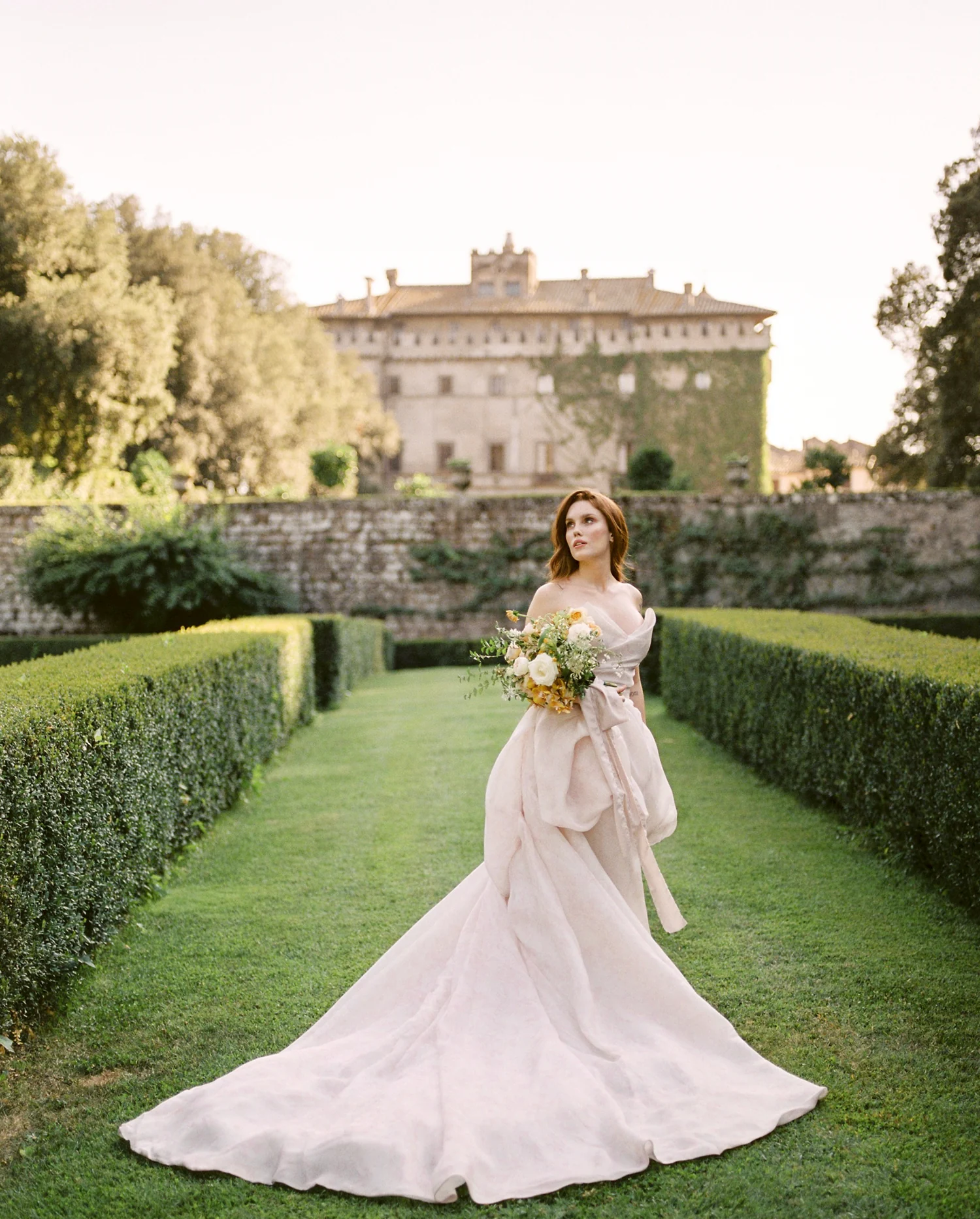 Bride in a blush gown on a hedge-lined lawn before a Tuscan villa